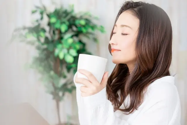 温かいお茶を両手で持って体を温めている女性