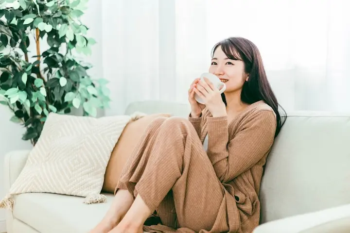 自宅のリビングで温かいハーブティーを飲みながら、秋バテ対策のセルフケア温活をしている女性