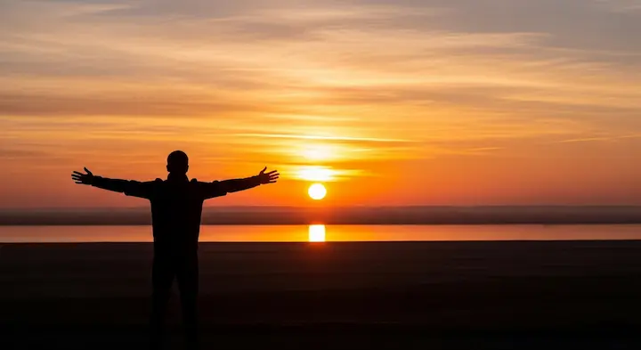 朝日が昇る美しい景色に向かって大きく深呼吸する人物のシルエット。温浴によって心身が整い、最高のコンディションで一日を始める様子を象徴している。